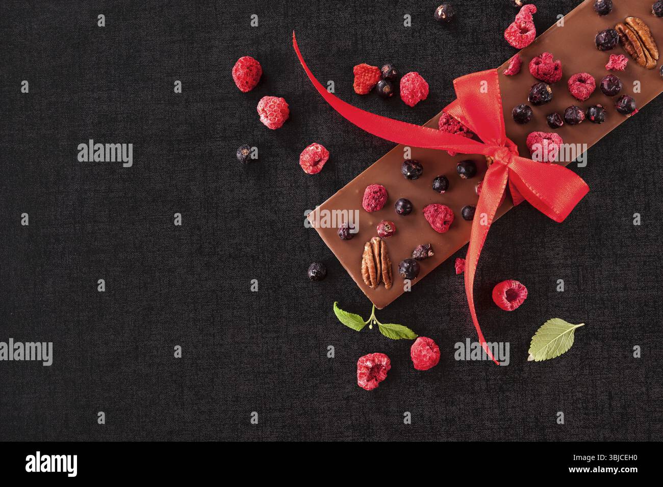 Luxuriöser Schokoladenriegel mit Band und gesunden gefriergetrockneten Beeren von oben mit Kopierraum Stockfoto