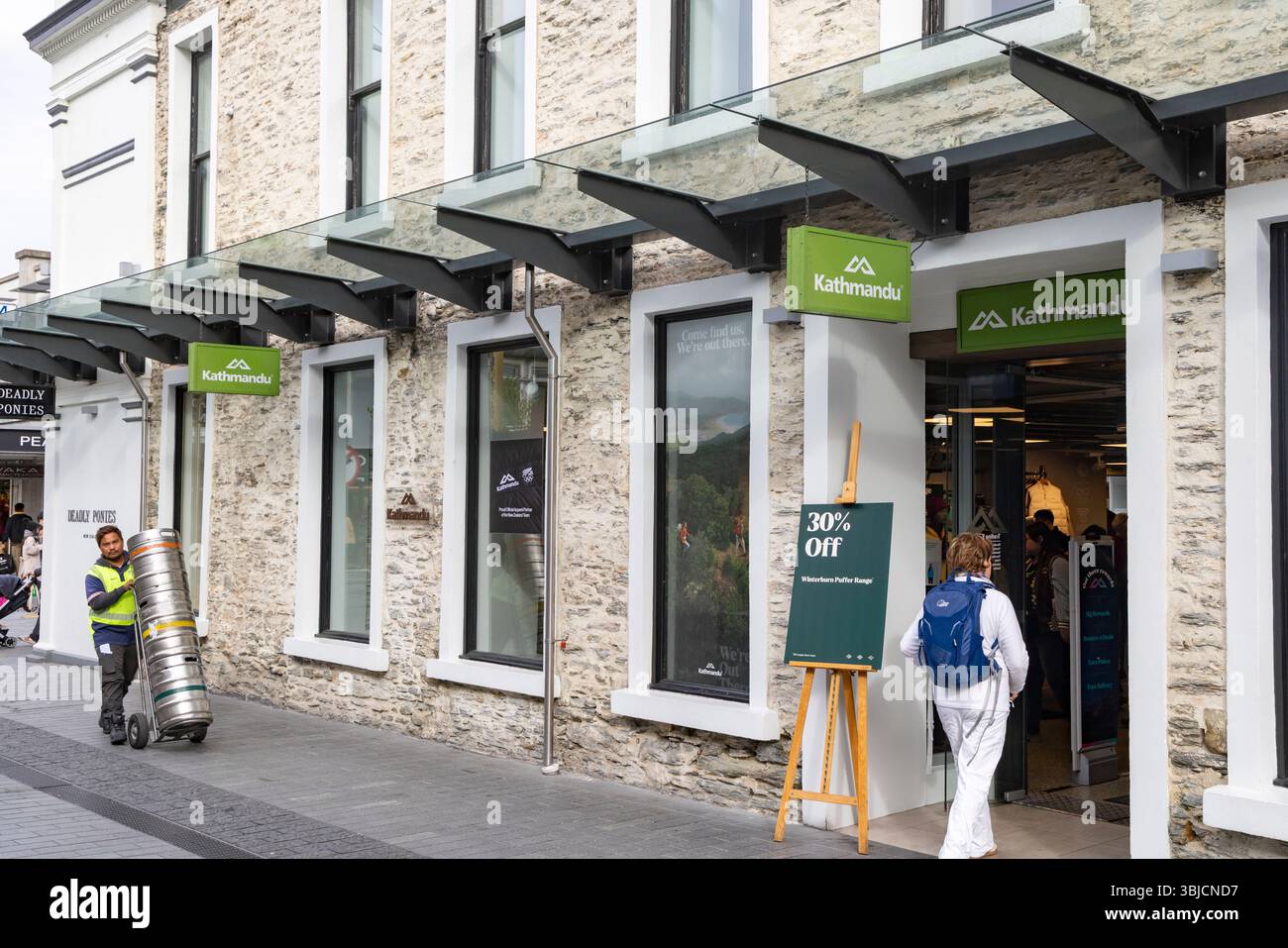 Kathmandu Outdoor-Bekleidungsgeschäft, Model entlassene Frau geht in das Bekleidungsgeschäft im Stadtzentrum von Queenstown, Otago, Südinsel, Neuseeland, 2025 Stockfoto