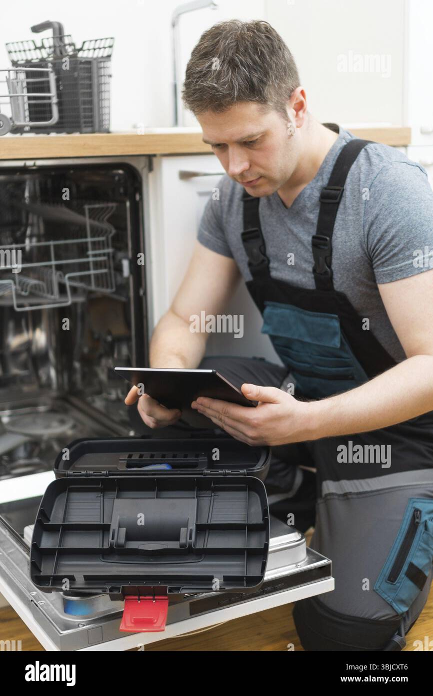 Handwerker mit Tablet-pc, der Haushaltsspülmaschine in der Küche repariert Stockfoto