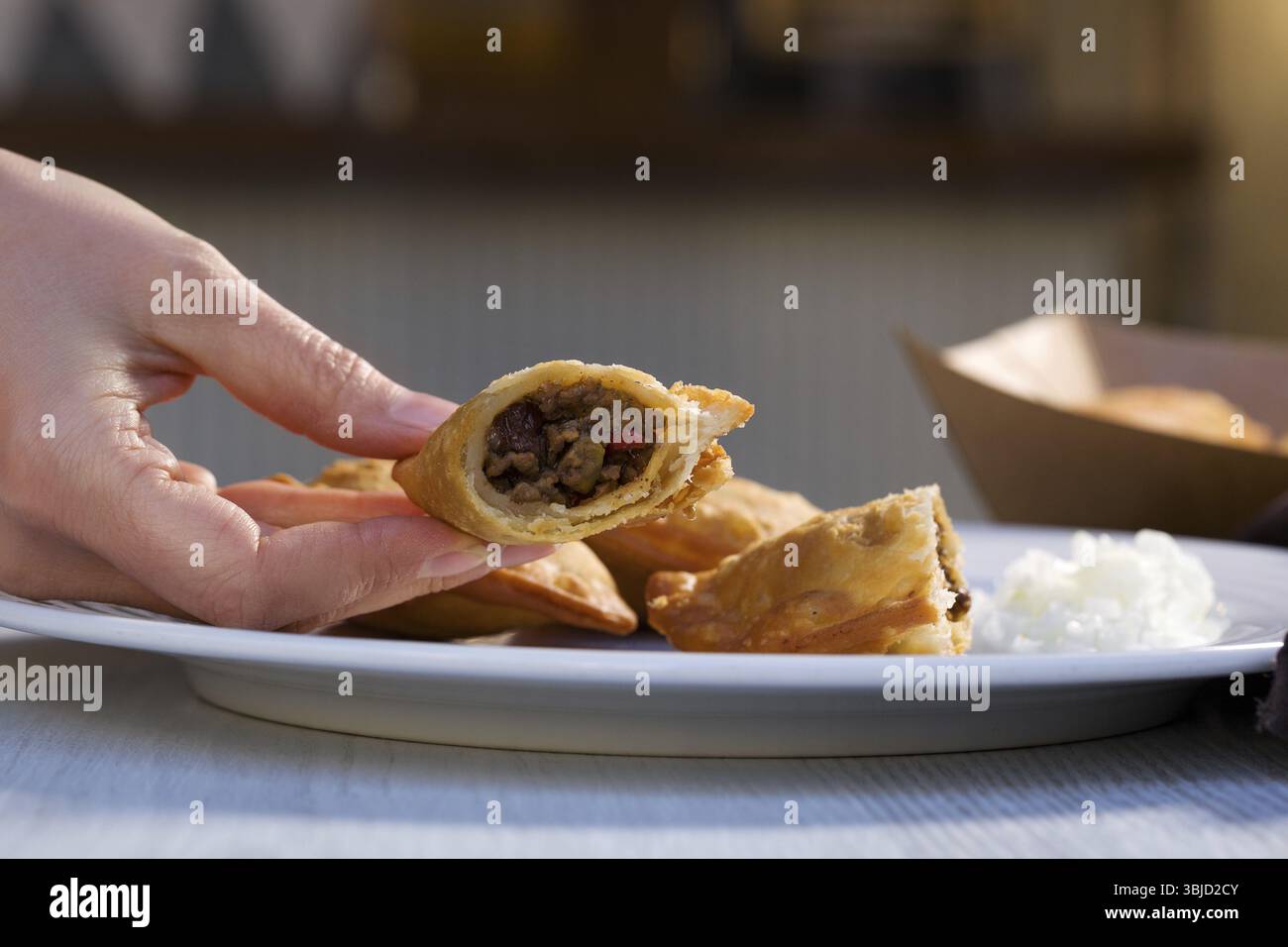 Traditionelles gebackenes argentinisches Empanadas herzhaftes Gebäck mit Fleisch-Rindfleisch-Füllung in Frauenhand auf weißem Teller Stockfoto