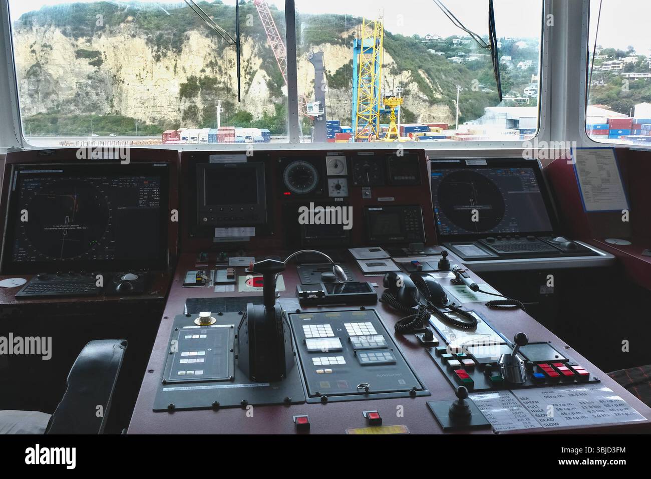Steuerkonsole der Schiffsbrücke mit Navigationsausrüstung und Stühlen des Containerschiffs mit Blick auf den Hafen von Napier. Stockfoto