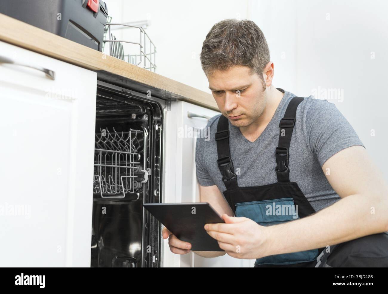 Handwerker mit Tablet-pc, der Haushaltsspülmaschine in der Küche repariert Stockfoto