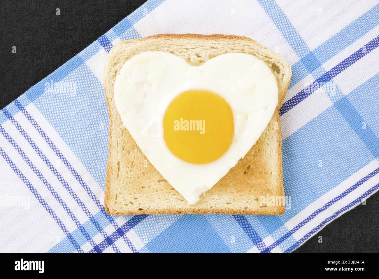 Sonniges Ei in Herzform auf Toast, Blick von oben. Ich liebe das Frühstück. Frische, moderne Bildsprache. Kulinarische Kunst Stockfoto