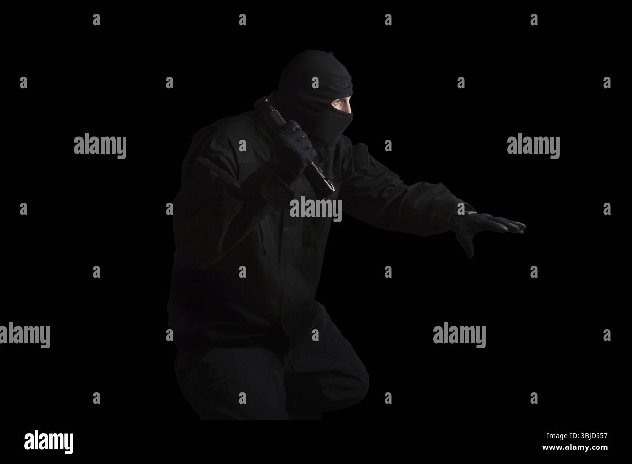 Mann in schwarzer Maske und schwarzem Tuch, der die Taschenlampe isoliert auf schwarzem Hintergrund hält. Gefährliche Kriminelle, die Verbrechen begehen Stockfoto