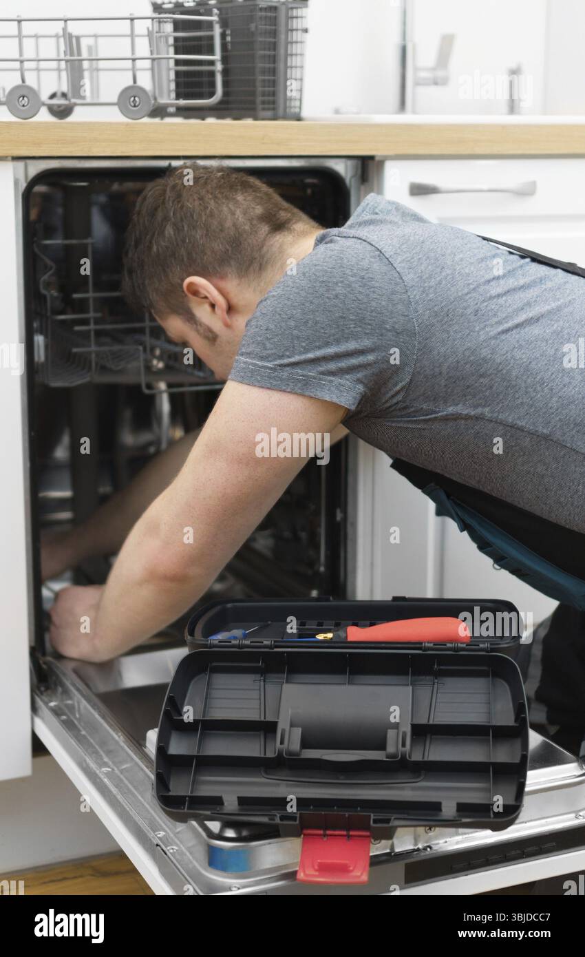 Professioneller Handwerker in Overalls, der Haushaltsspülmaschine in der Küche repariert Stockfoto