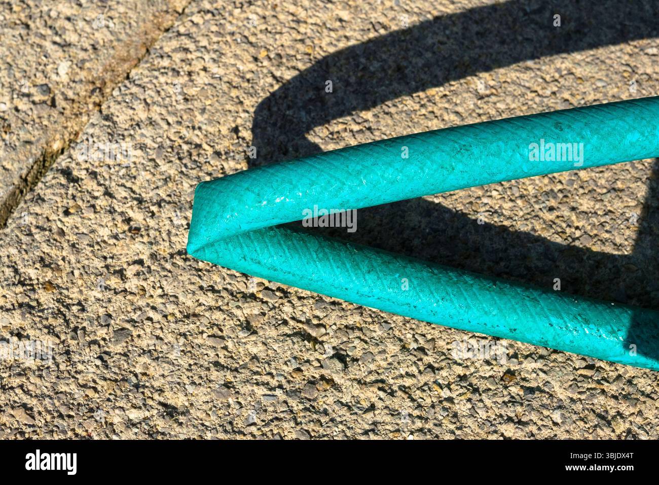 Grüner Gartenschlauch mit Knickschutz Wasserfluss scharfes Licht starker Schatten Wasser kann nicht passieren Stockfoto
