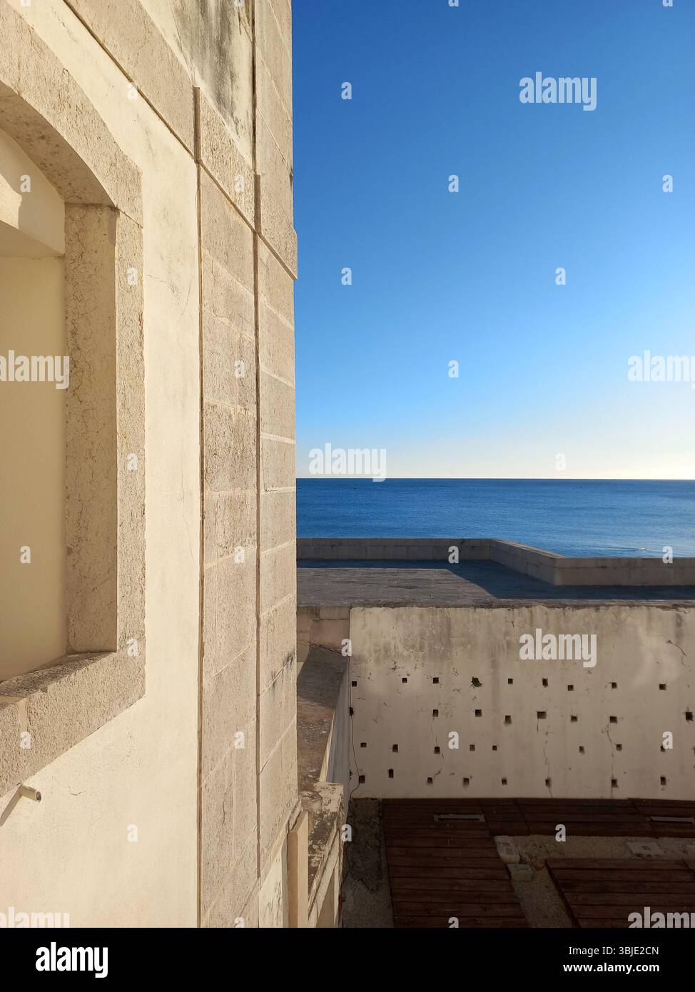 Sonnenlicht leuchtet auf den Wellen des Atlantiks, während sie sanft den goldenen Sandstrand von Sesimbra erreichen, der von einem Aussichtspunkt an der Küste erfasst wird. Stockfoto