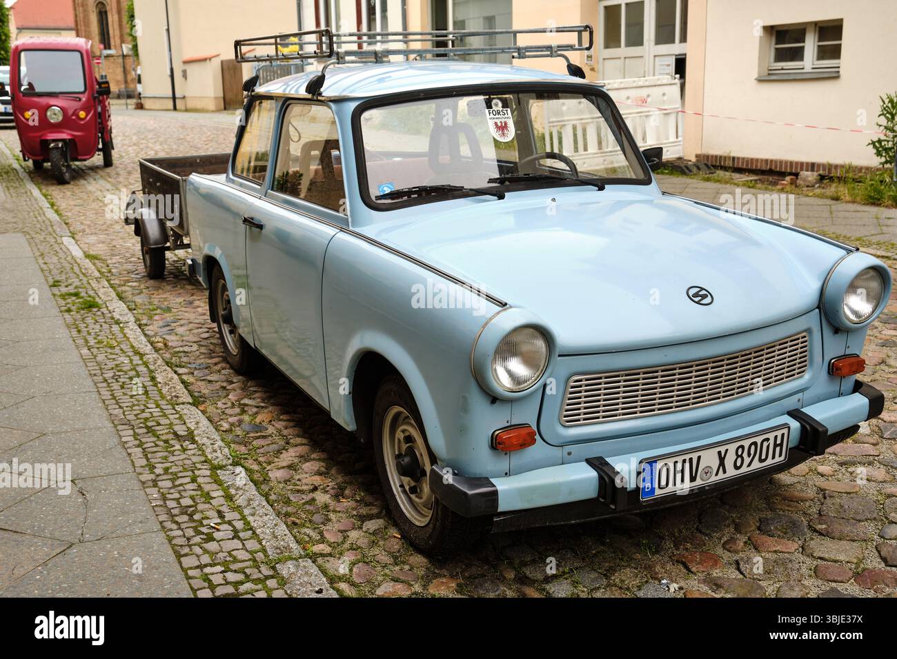 10. Juni 2025 - Fürstenberg-Deutschland: Hellblauer Trabant mit Anhänger auf Kopfsteinpflasterstraße im historischen ostdeutschen Fürstenberg, NOR Stockfoto