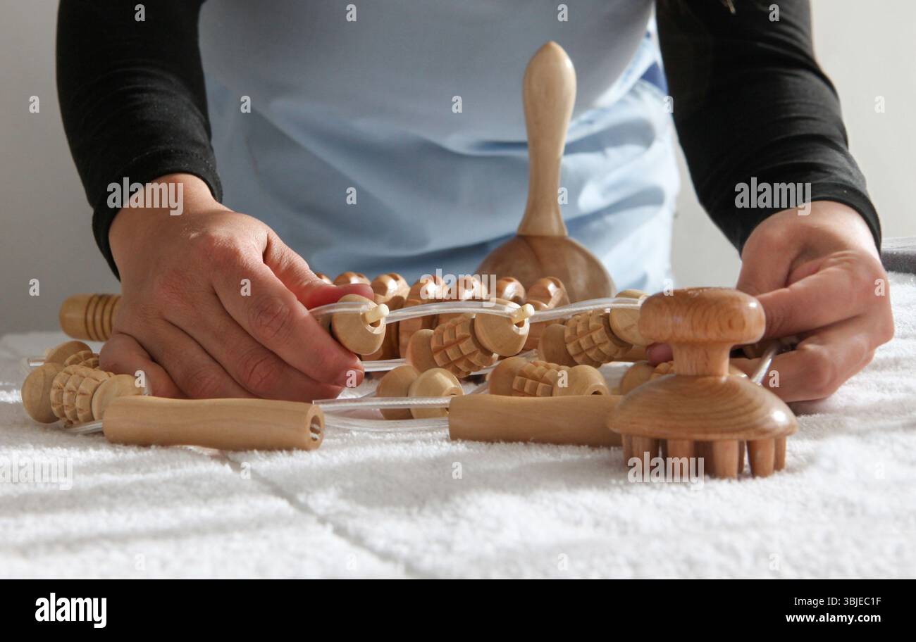 Hispanische Massagetherapeutin in professioneller Uniform, die Holzmassagewerkzeuge wie Rollen, Pilze auf einer Massagetabelle vorbereitet und organisiert Stockfoto