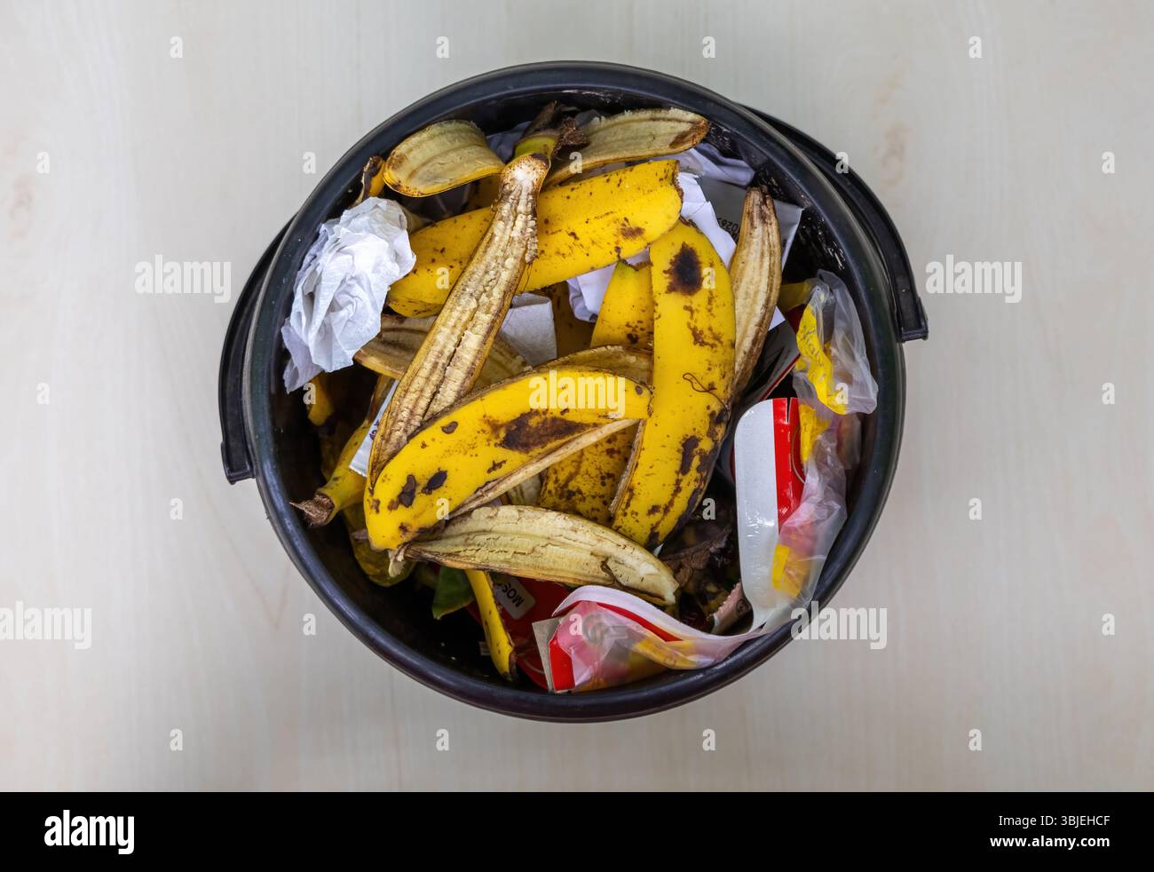 Schwarzer Eimer gefüllt mit verschiedenen Haushaltsabfällen. Enthält Lebensmittelreste, Papier, Kunststoff. Blick von oben auf Hausmüll. Abfallbehälter. Stockfoto