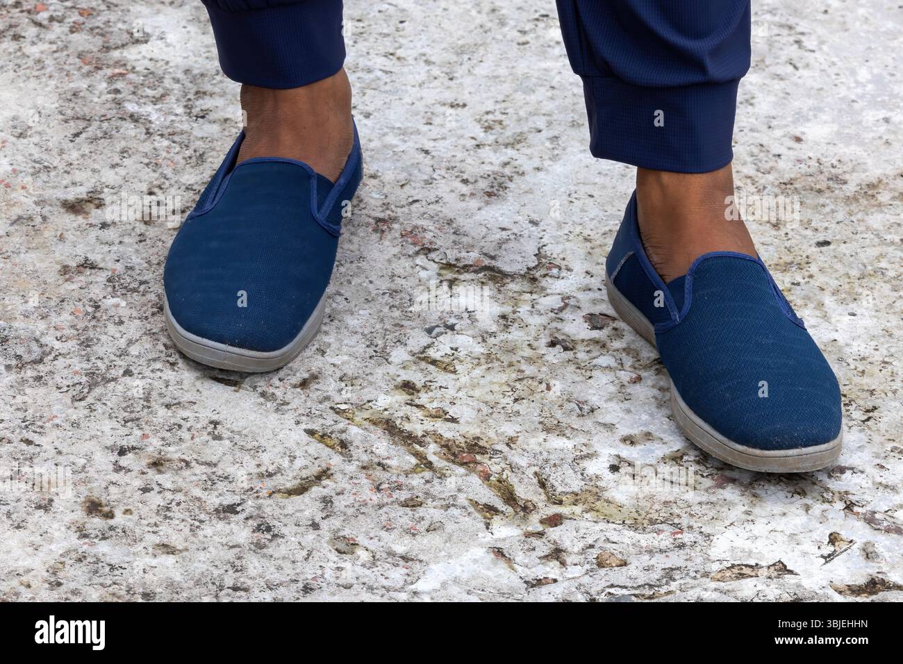 Männlicher Fuß in marineblauen Turnschuhen auf Beton. Stylische, modische, bequeme Schuhe, Nahaufnahme Herrenschuhe. Stockfoto