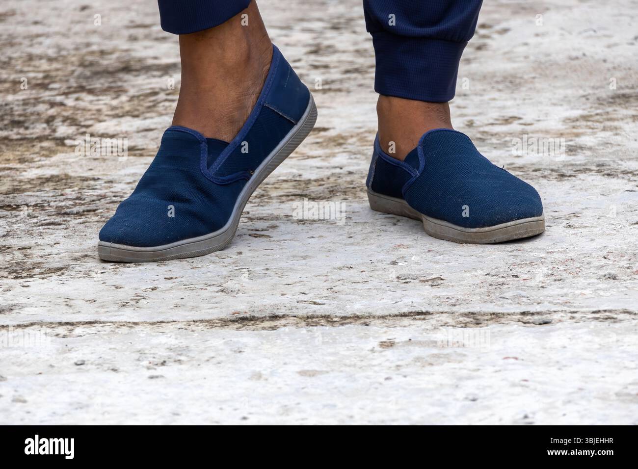 Nahaufnahme des Fußes des Mannes mit marineblauen Turnschuhen auf Beton. Bequeme, stylische, sportliche Schuhe. Stockfoto