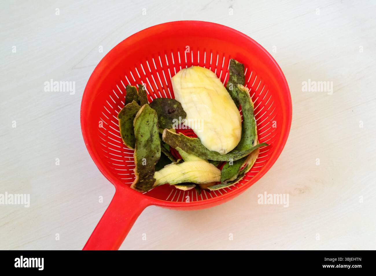 Nach dem Verzehr einer Reifen Mango, grüner Haut und großer Samen auf einem roten Plastikkorb, hellem Holz. Stockfoto