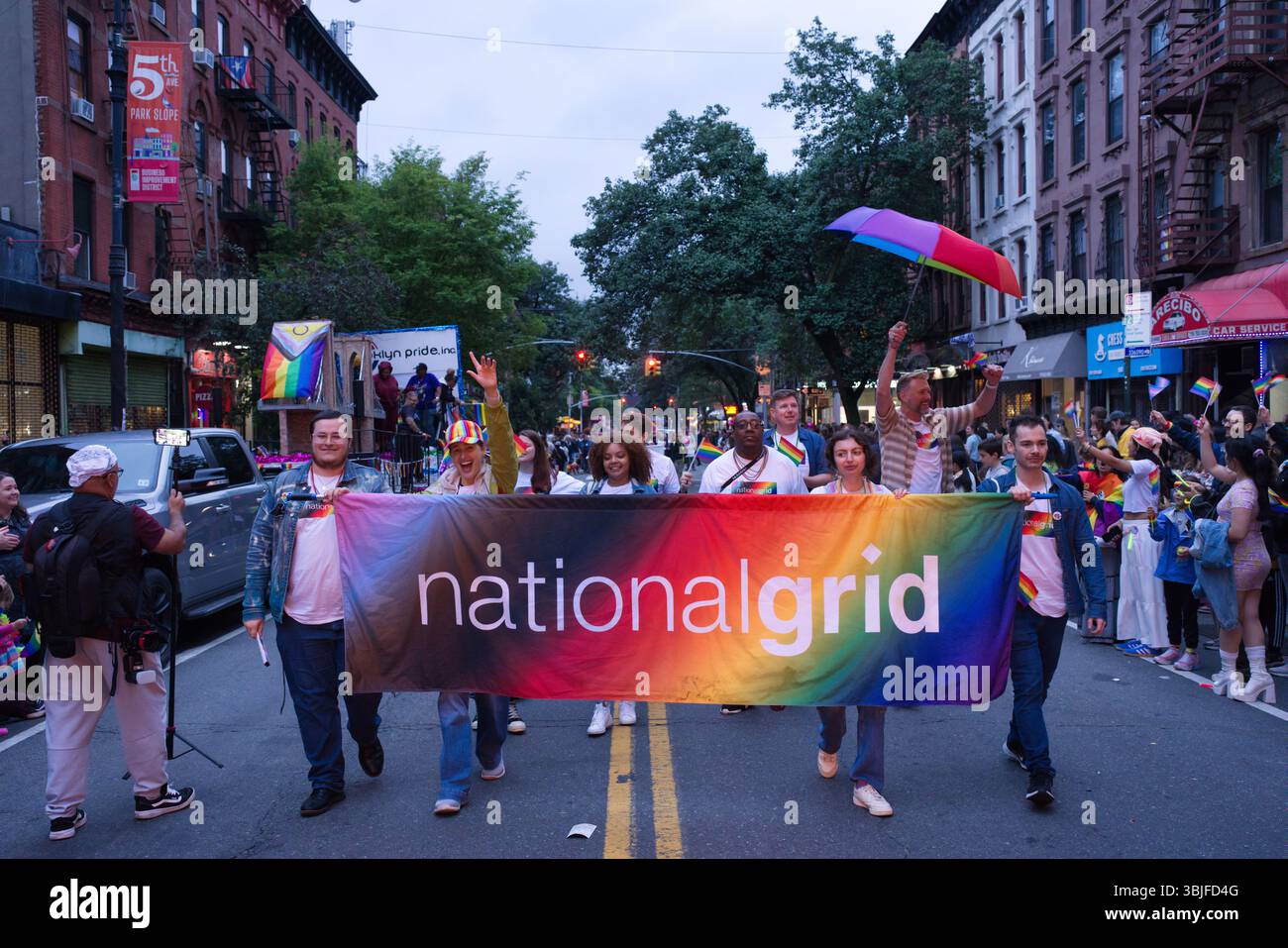 Eine vielfältige Gruppe von Menschen marschiert in einer Pride-Parade mit einem großen Regenbogenbanner mit dem Aufdruck „Nationalgrid“. Die Parade findet in einer Stadt statt Stockfoto