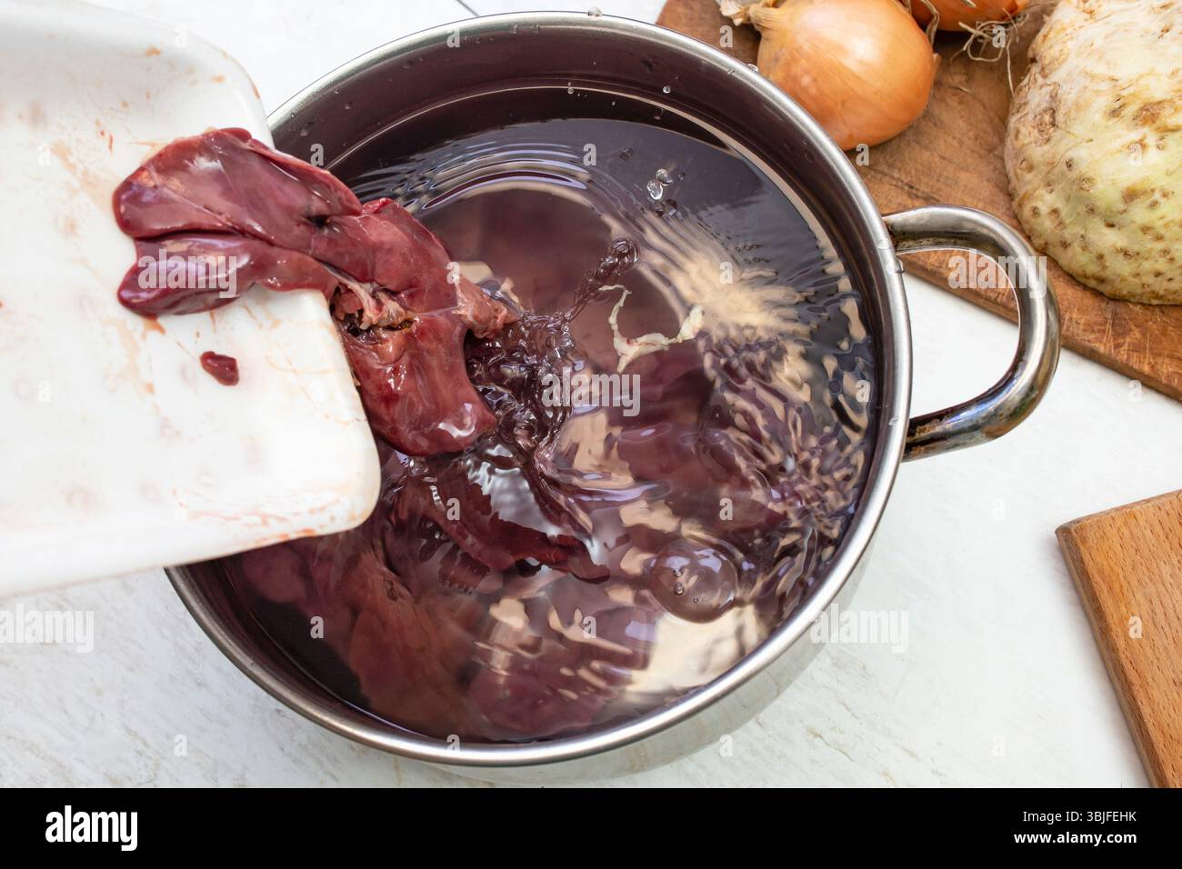 Hühnerleber in einen mit kaltem Wasser gefüllten Topf zum Waschen vor dem Kochen gießen, weicher Fokus in Nahaufnahme Stockfoto
