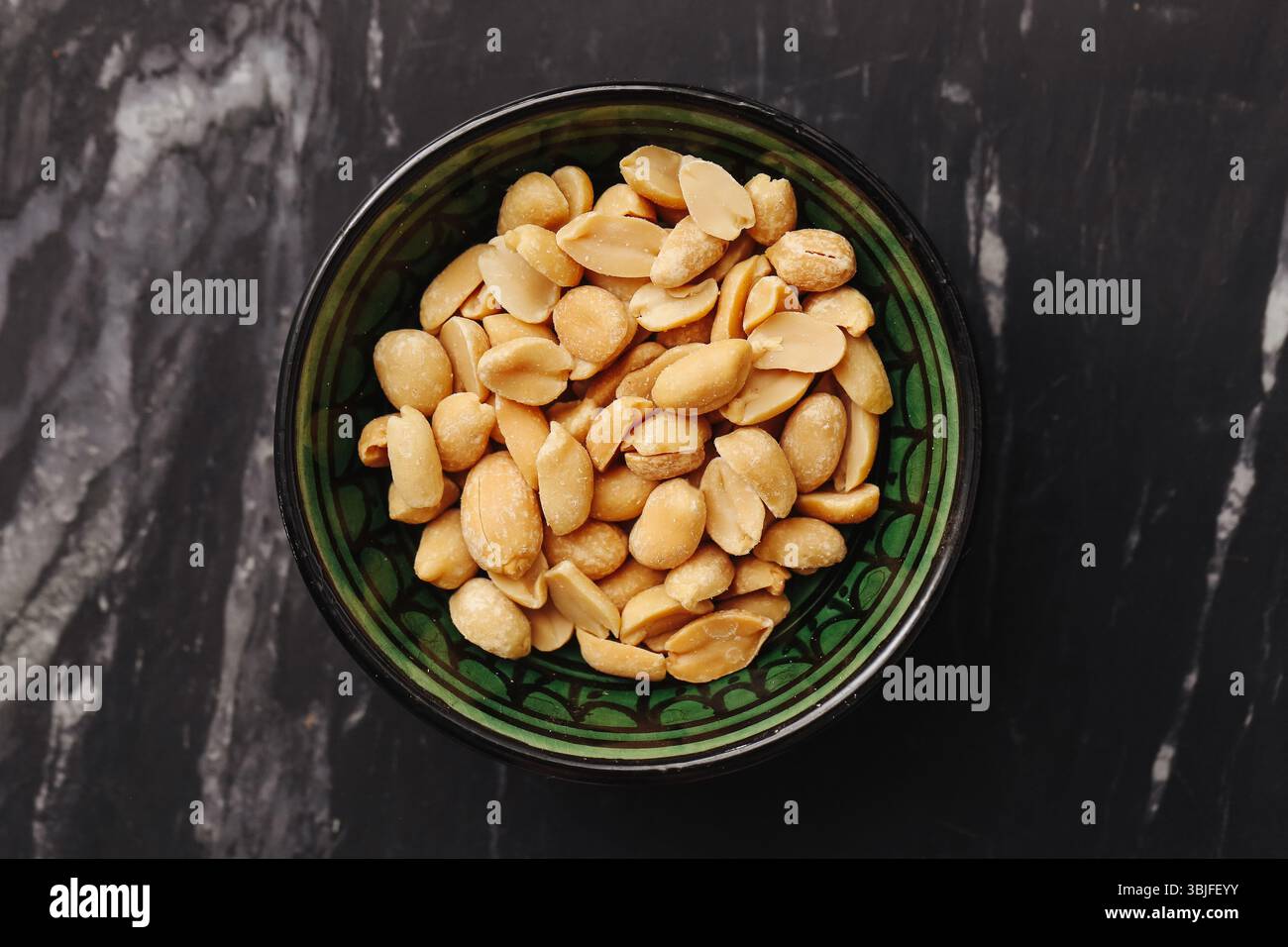 Gesalzene Erdnüsse in einer Schüssel. Goldener gerösteter Snack. Gesundes veganes Protein. Marmorhintergrund flach. Organische knusprige Textur. Energiereiche Lebensmittel. Stockfoto
