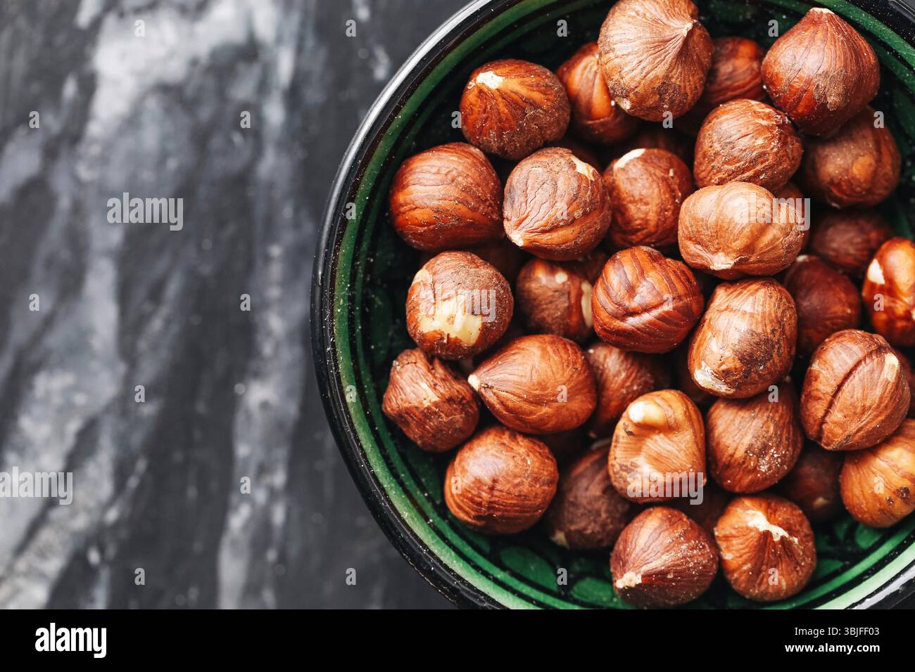 Haselnüsse in grüner Schüssel. Braune Nüsse Nahaufnahme. Hintergrund mit Marmorstruktur. Gesunder pflanzlicher Snack. Organische Proteinquelle. Veganes Essen. Stockfoto