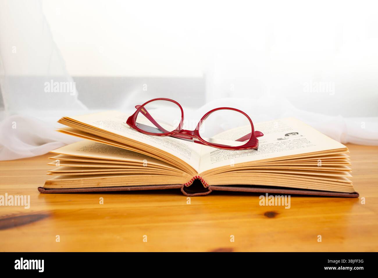 Das Buch wurde auf einem Holzschreibtisch mit sonnigem Fensterhintergrund geöffnet und bietet einen Hintergrund für Bibelstudien Stockfoto