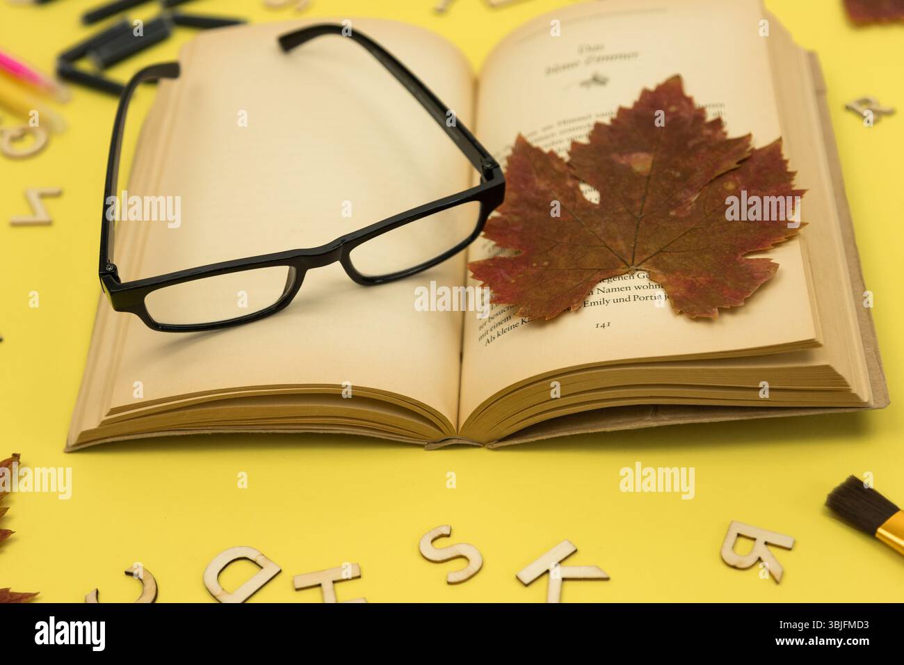 Herbstlich getrocknetes Ahornblatt, offenes Buch und Lesebrille. Nostalgie. Herbst Hintergrund Stockfoto