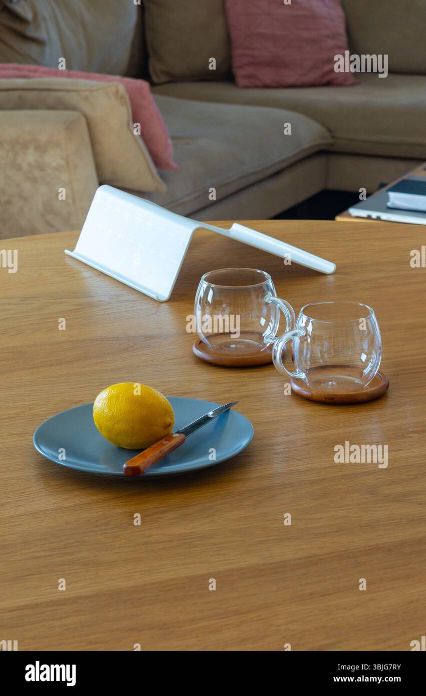 Stillleben Komposition mit frischer Zitrone, Messer und leeren Glasbechern auf einem Holztisch in gemütlicher Küche. Seitenansicht mit Tageslicht Stockfoto