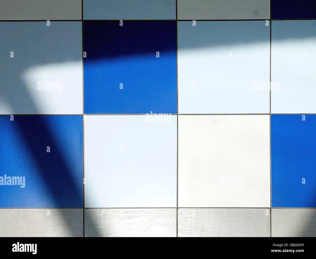 Leuchtende farbige Fliesen bilden ein optisch ansprechendes Muster auf dem Boden, während kontrastierende Schatten ihr Design hervorheben. Das Zusammenspiel von Licht erzeugt Stockfoto