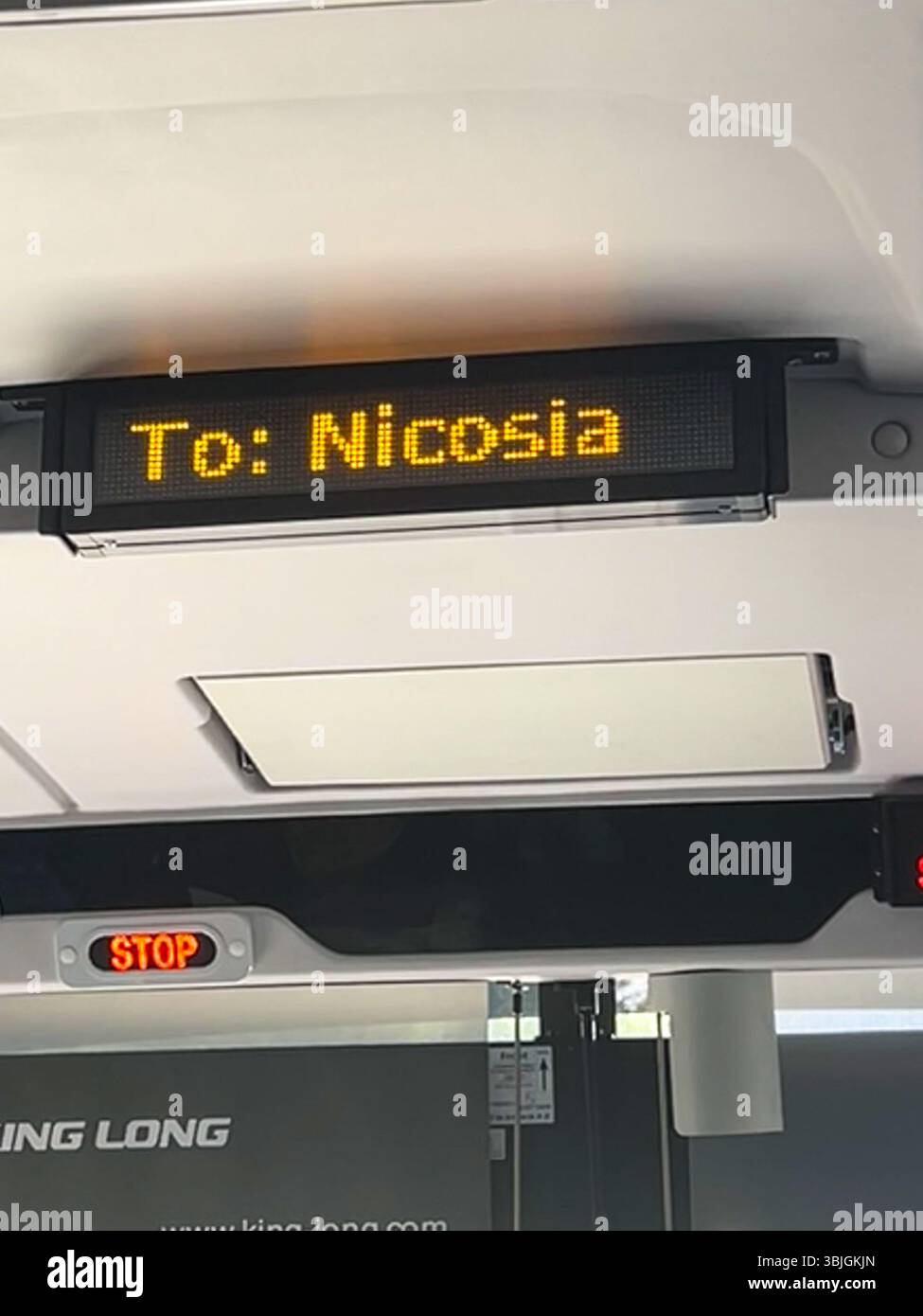 Innenraum eines modernen Busses mit einem hellen LED-Schild, das das Ziel „nach Nicosia“ anzeigt, und einer beleuchteten roten Stopptaste, die während der Tagesfahrt erfasst wird. - Smartphone-aufgenommenes Stockfoto