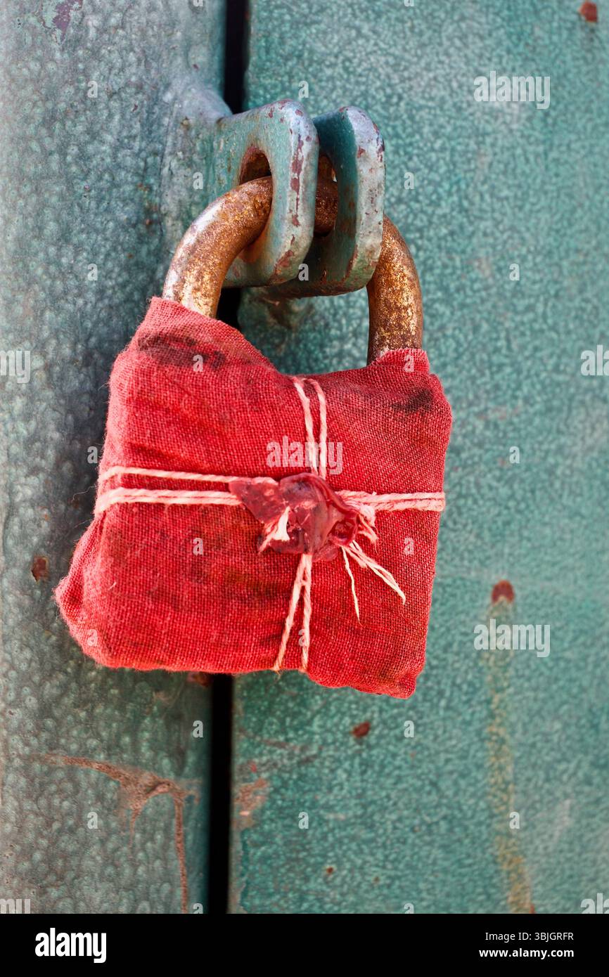 Ein Vorhängeschloss in rotes Tuch gewickelt und mit Wachs und Schnur versiegelt, symbolisch an einer grünen Metalltür in Rajshahi, Bangladesch befestigt. Stockfoto