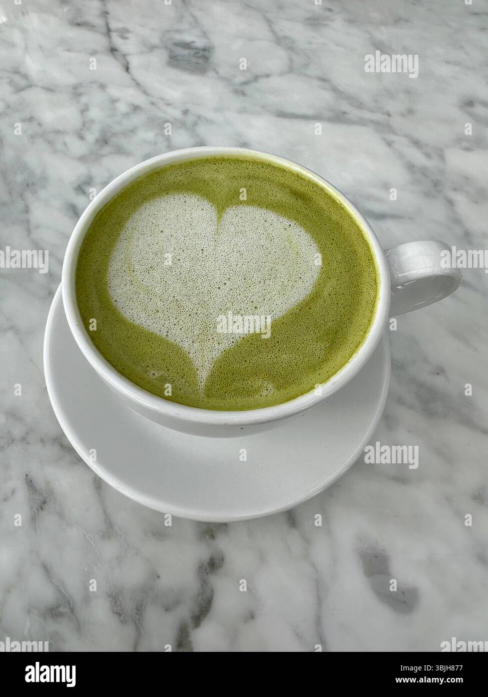 Heißer Matcha mit Herz Latte Art auf Marmorhintergrund - Smartphone-aufgenommenes Stockfoto