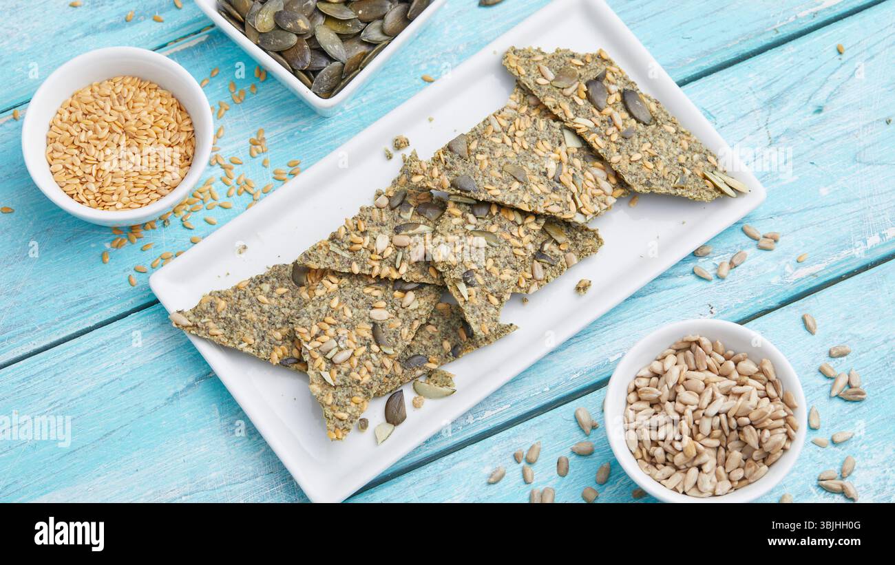 Seed Cracker mit Sonnenblumenkernen auf weißem Teller – ein gesunder, knuspriger Snack oder ein leichtes Mittagessen, mit einem weichen blauen Hintergrund für sauberes Essen. Stockfoto