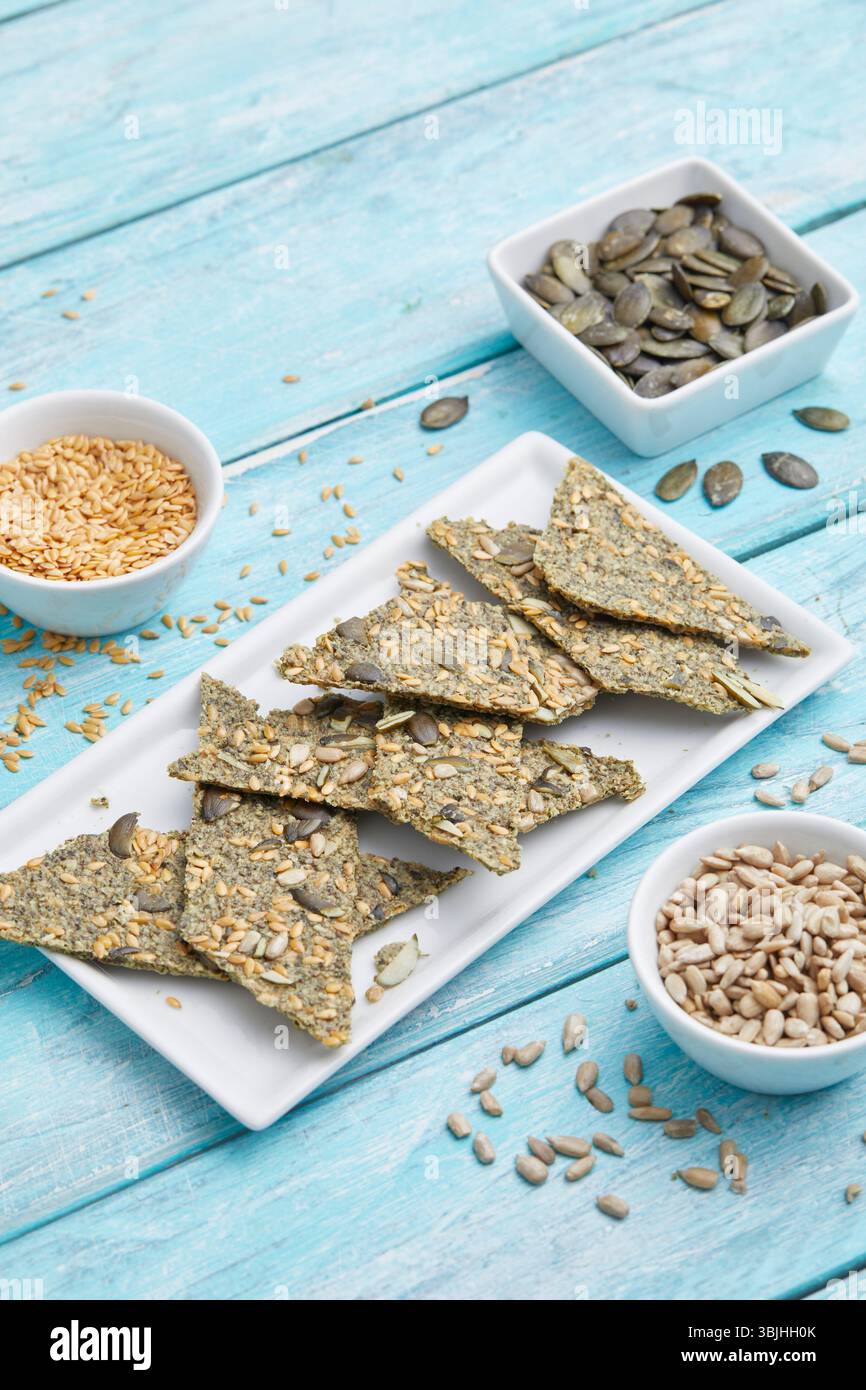 Seed Cracker mit Sonnenblumenkernen auf weißem Teller – ein gesunder, knuspriger Snack oder ein leichtes Mittagessen, mit einem weichen blauen Hintergrund für sauberes Essen. Stockfoto