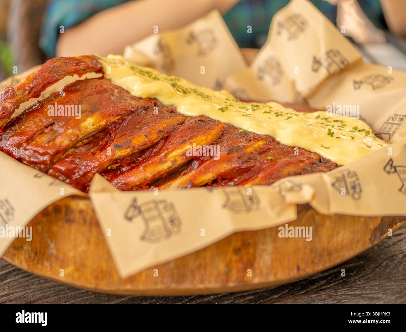 Köstliche Schweinerippchen mit gelber Senfsoße, serviert auf einem in Streifen geschnittenen und in braunes Papier gewickelten Teller für die Präsentation des Restaurantmenüs Stockfoto