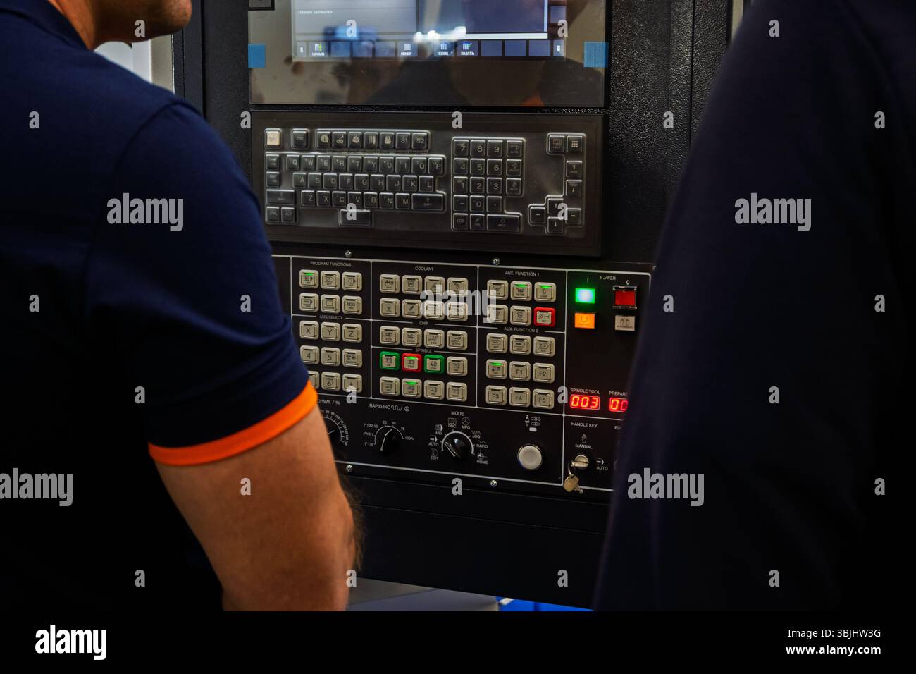 Zwei Personen stehen zusammen neben einer Industriemaschine mit einem Bedienfeld mit vielen Tasten. Stockfoto