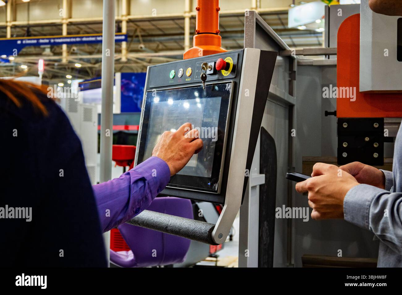 Industriearbeiter, der CNC-Maschinensteuertafel mit Touchscreen-Schnittstelle auf der Fertigungsmesse bedient. Moderne automatisierte Geräte mit digitaler Technologie Stockfoto