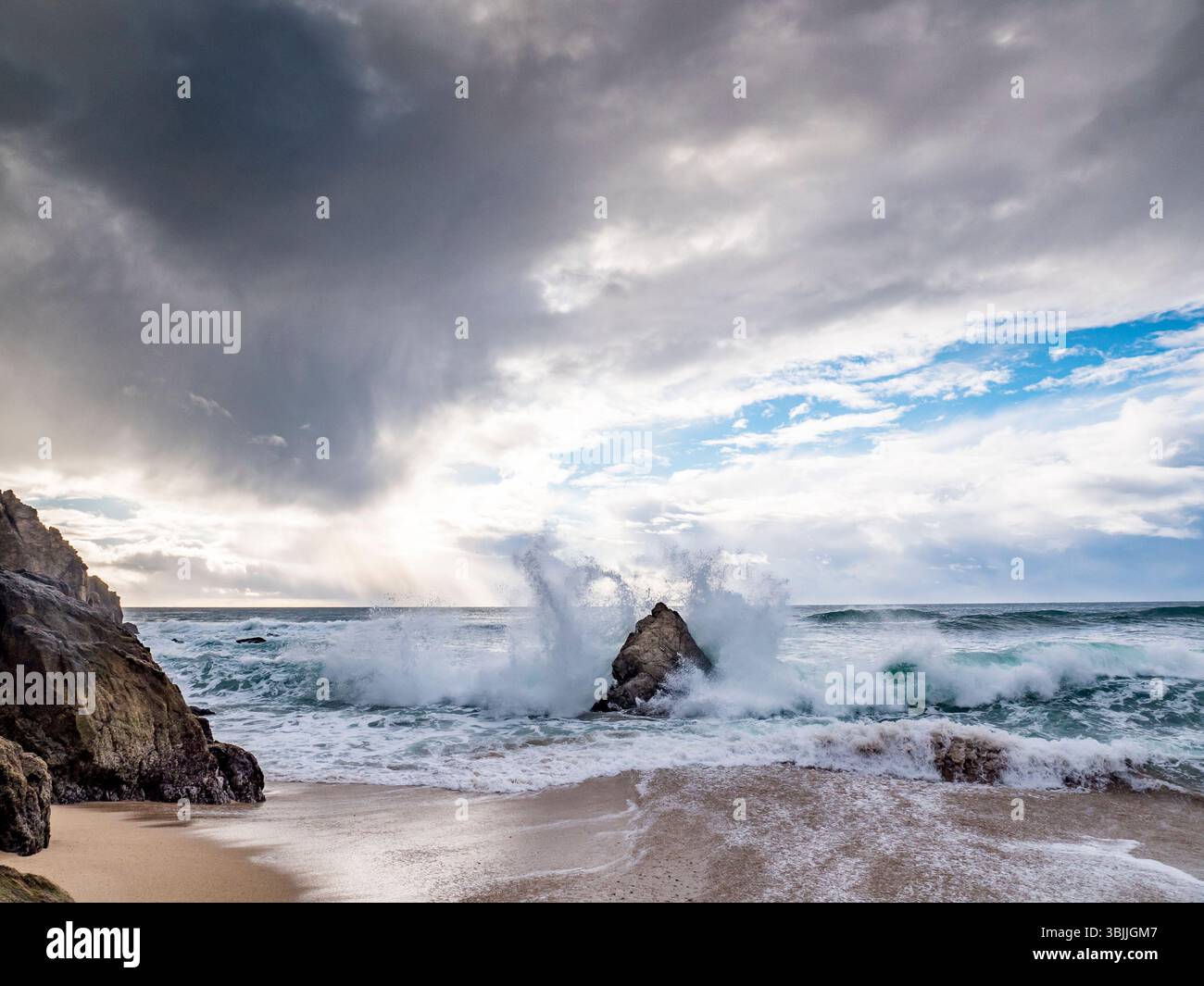 Die Welle stürzt auf den Felsen in der Nähe des goldenen Sandstrandes Stockfoto