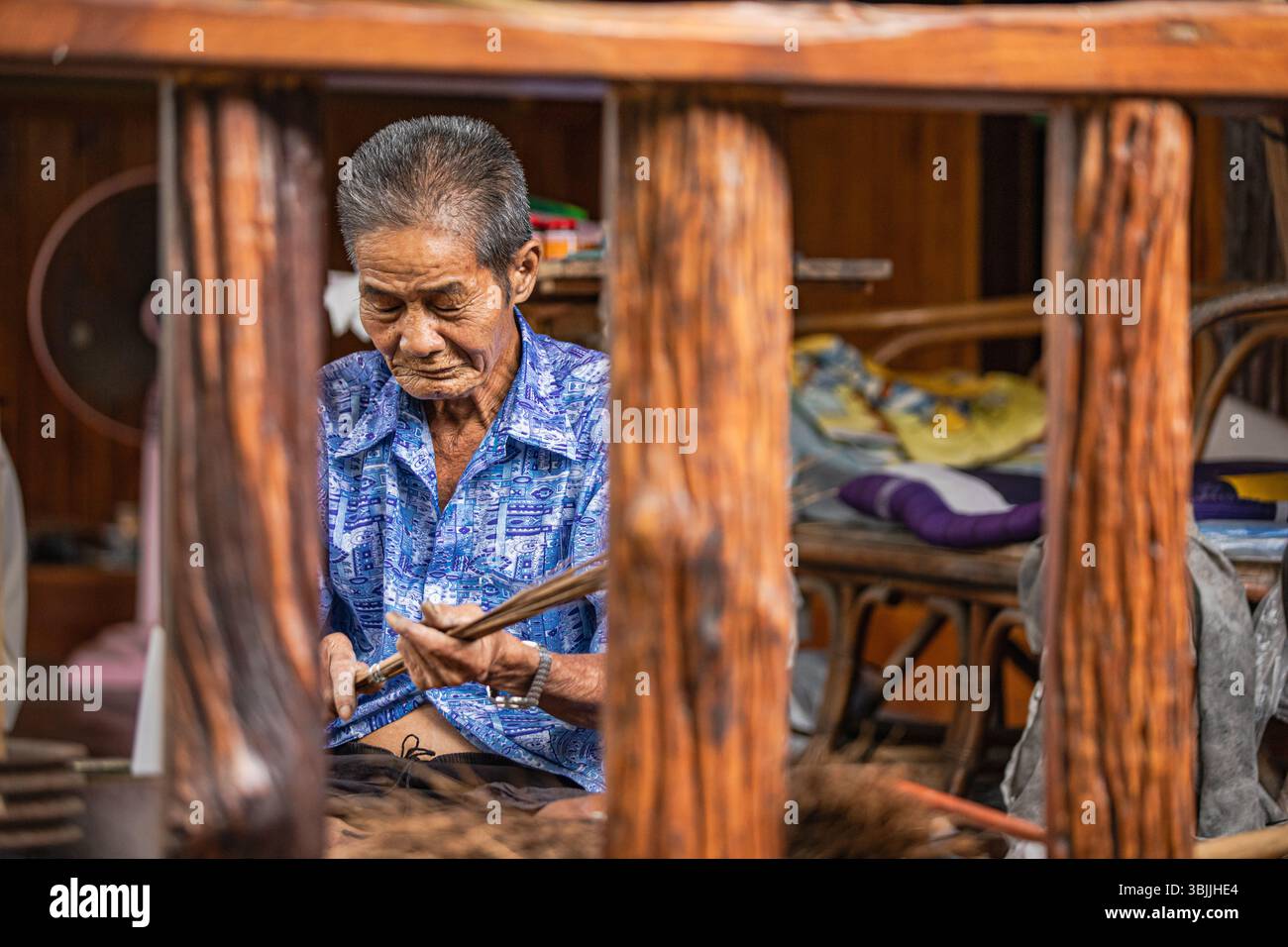 Älterer Thai-Mann, der Besen in einem traditionellen Holzhaus bastelt Stockfoto