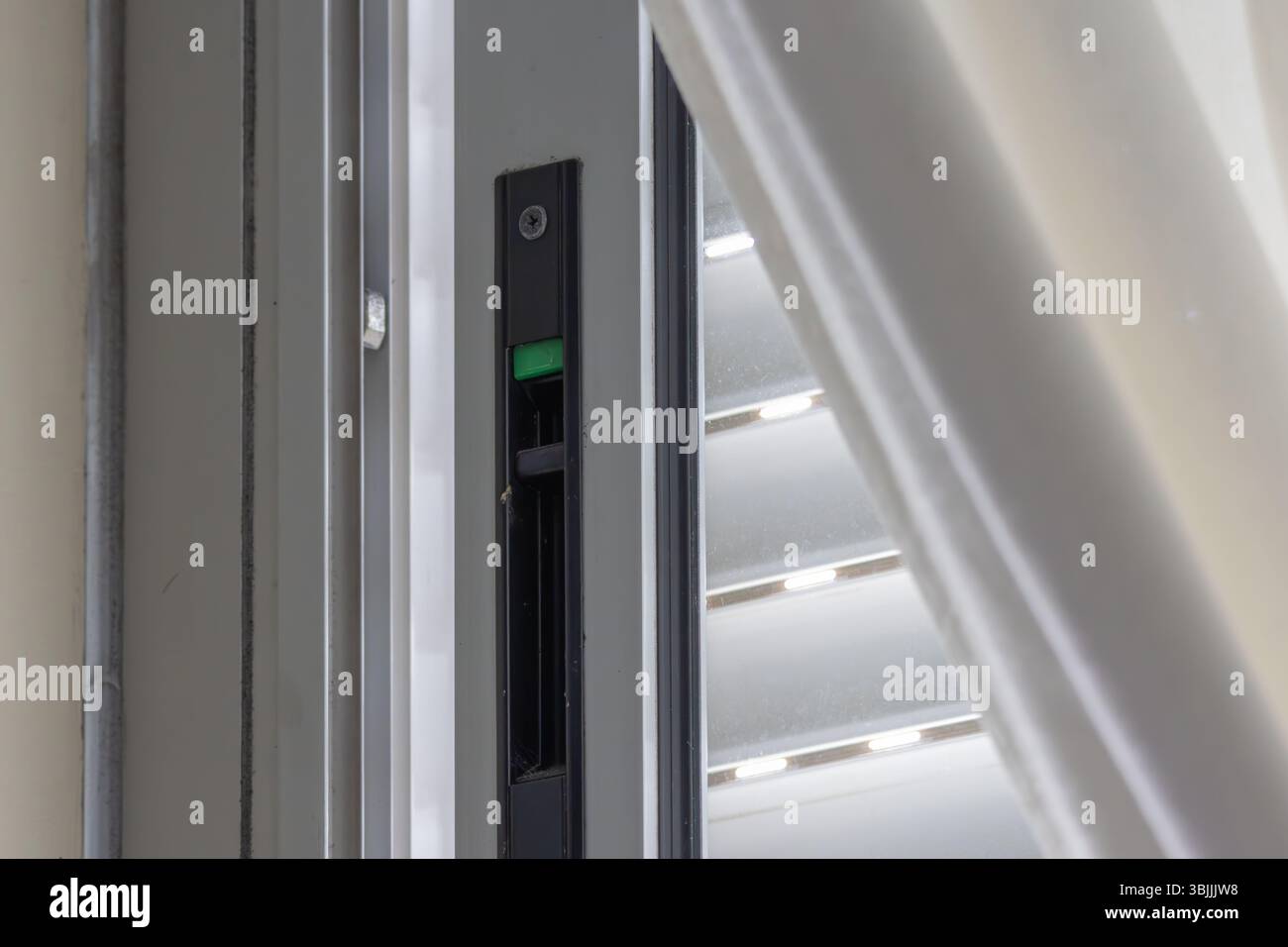 Die grüne Taste am Fensterschloss zeigt einen sicheren Zustand an, während die venezianischen Jalousien Privatsphäre und Lichtsteuerung bieten Stockfoto