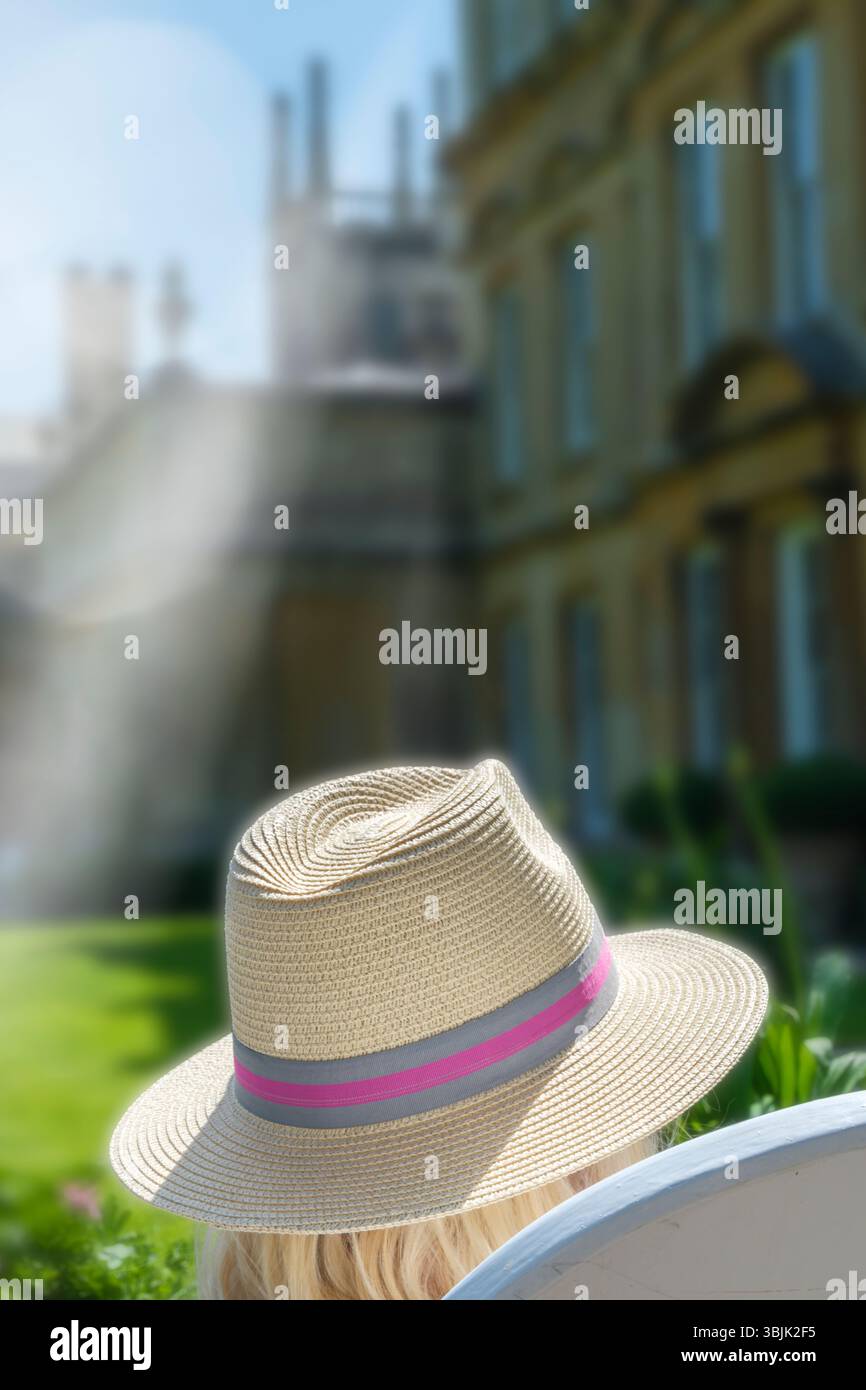 Badminton, Gloucestershire - Eine blonde Dame entspannt sich in der Sommersonne auf dem Gelände eines Herrenhauses mit Panamahut. Stockfoto