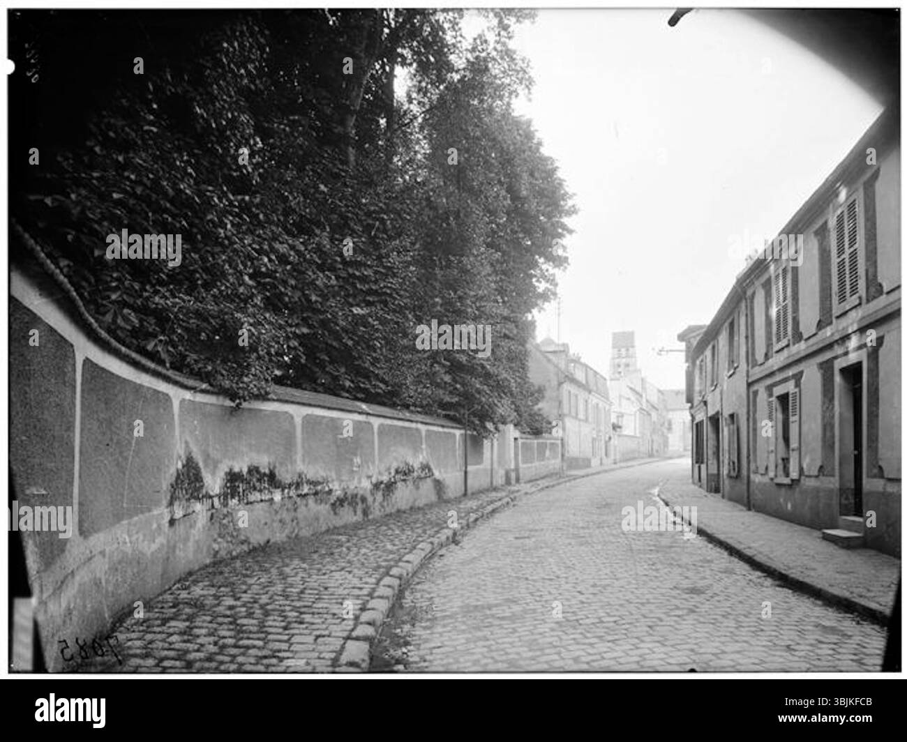 Eugène Atget fotografiert 1925 die Straßenfassade von Wissous, im Hintergrund ist der Glockenturm der Eglise Saint-Denis zu sehen. Das Foto ist eine historische Darstellung des Straßenlebens und der Architektur im Frankreich des frühen 20. Jahrhunderts. Stockfoto