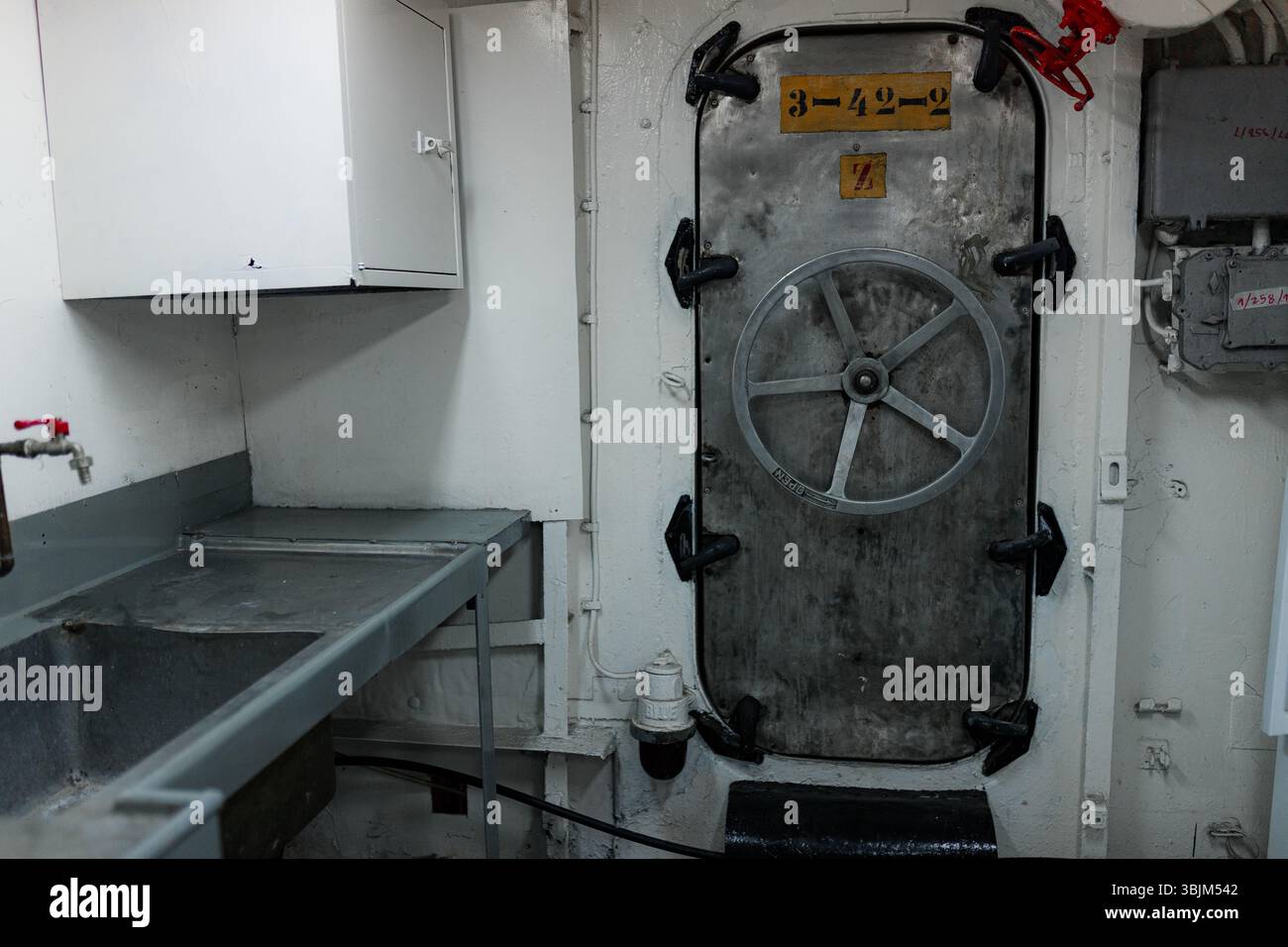 Innenraum für Industrieschiffe mit Metalltür und schwerem Radgriff bei schlechten Lichtverhältnissen. Stockfoto