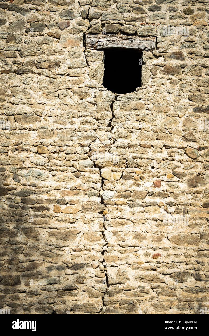 Eine verwitterte Steinmauer zeigt einen markanten Riss, der vertikal verläuft und ein kleines Fenster aufweist. Stockfoto Eine verwitterte Steinmauer zeigt einen markanten Riss, der vertikal verläuft und ein kleines Fenster aufweist. Stockfoto