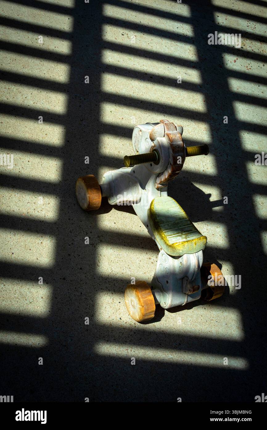 Ein Vintage-Spielzeugmodell sitzt auf einer Betonoberfläche, beleuchtet von Sonnenlicht, das durch eine Lattenstruktur strömt Stockfoto