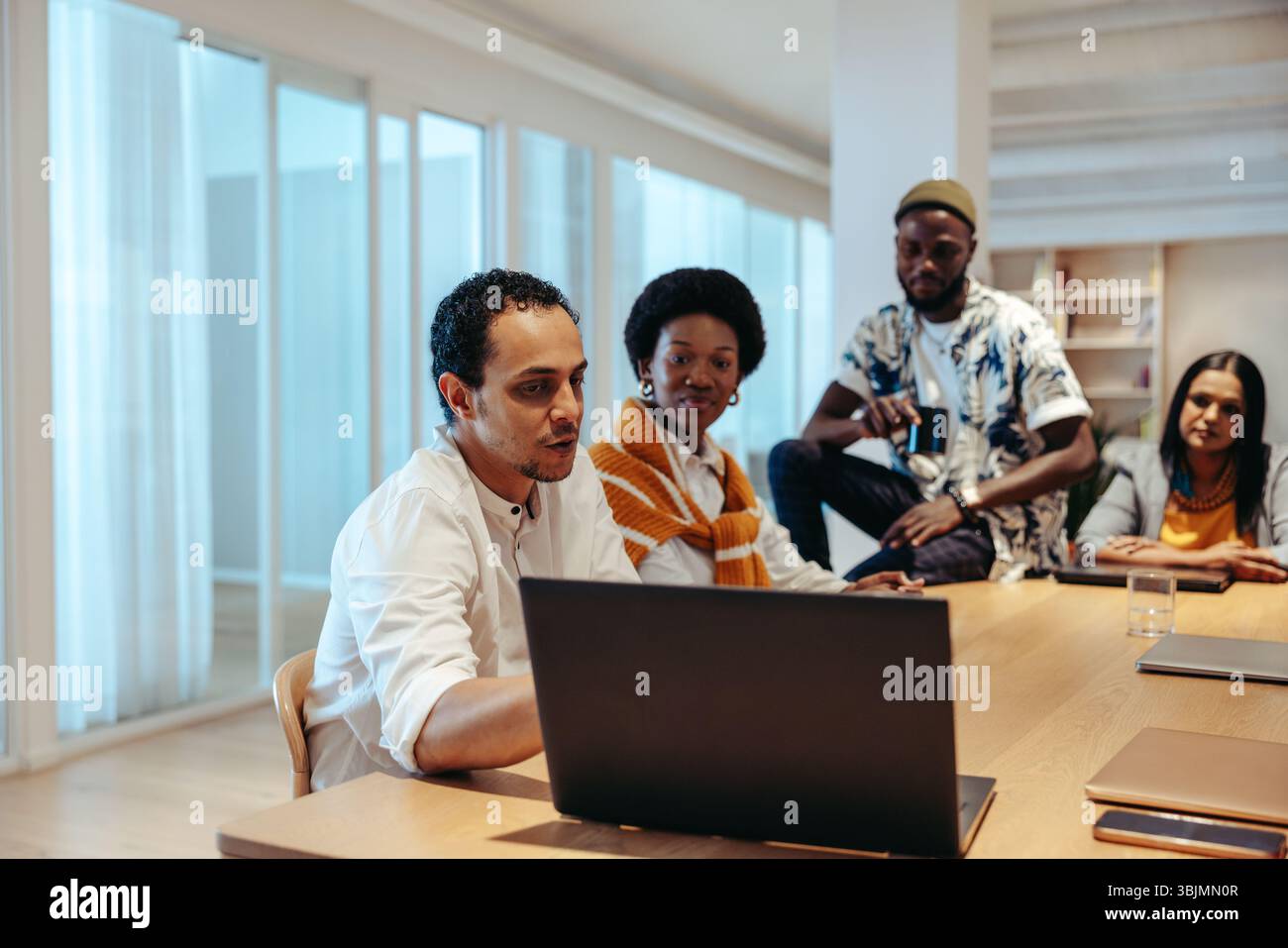 Ein vielseitiges Team von Fachleuten führte eine konzentrierte Diskussion über einen Marketingplan in einer modernen Büroumgebung. Die Gruppe arbeitet um eine Runde zusammen Stockfoto