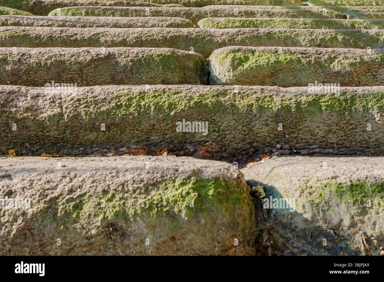 Verwitterte Steinstufen, reich an Textur und bedeckt mit Flecken aus grünem Moos, steigen einen Hügel unter weichem natürlichem Licht hinauf. Die unebene Oberfläche deutet darauf hin Stockfoto