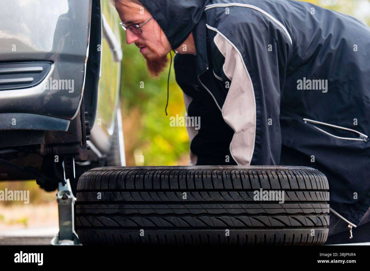 Junger Erwachsener, der das Rad eines Autos inspiziert Stockfoto