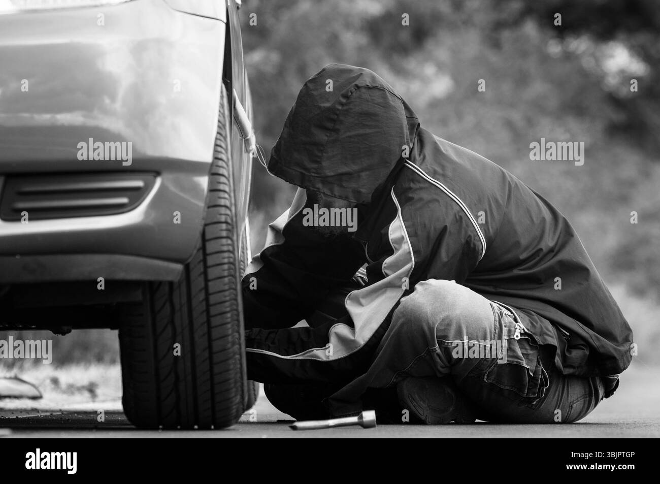 Junger Erwachsener, der das Rad eines Autos inspiziert Stockfoto