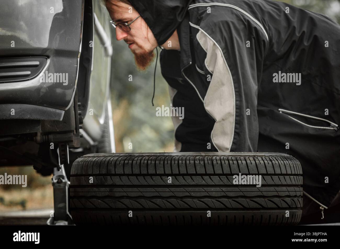 Junger Erwachsener, der das Rad eines Autos inspiziert Stockfoto