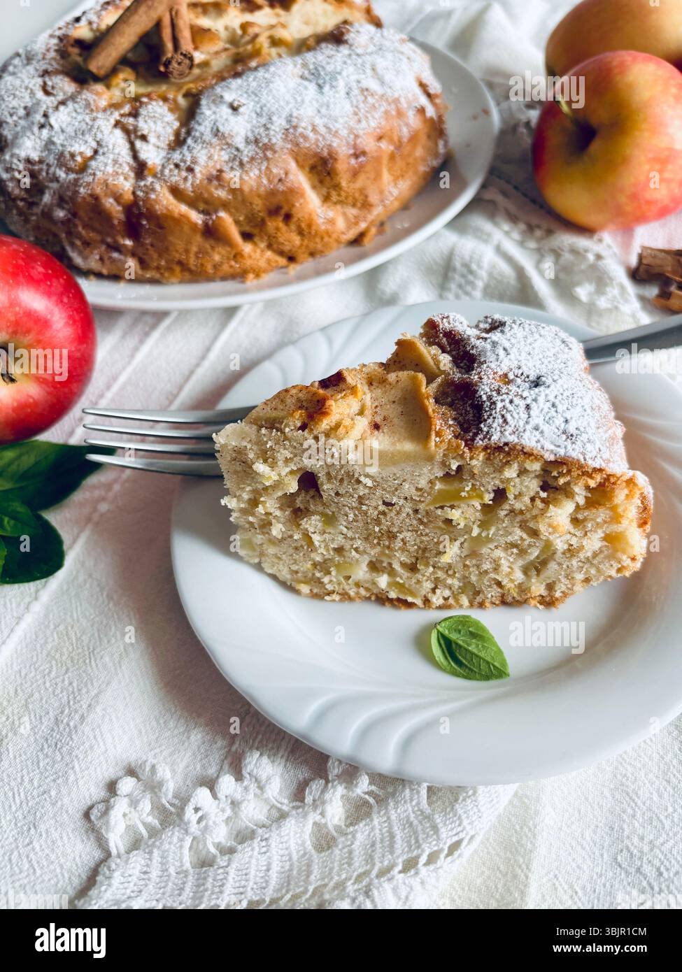 Ein Stück köstlicher hausgemachter Apfelkuchen, dekoriert mit Zimtstangen und frischen Äpfeln im Hintergrund. Direkt darüber. Stockfoto