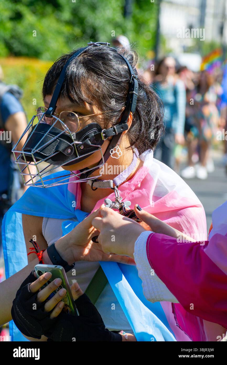 Ein Transgender-Teilnehmer, der eine Maske trägt und mit einer Trans-Stolz-Flagge versehen ist, erhält ein temporäres Tattoo bei der Warschau Pride Parade in Warschau, Polen 2025 Stockfoto