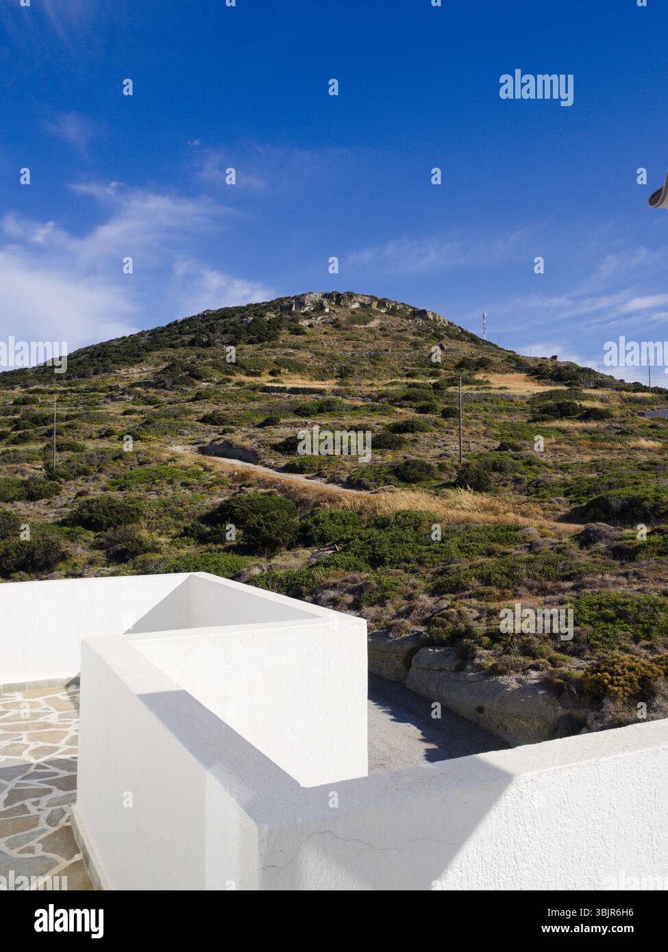 Traditioneller griechischer Balkon in heller Sonne mit trockenem Hügel und lebendigem blauem Himmel, der eine klassische griechische Insel-Sommeratmosphäre zeigt. Stockfoto