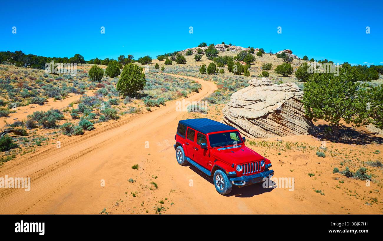 Roter SUV auf der gewundenen Desert Road mit Felsformationen und Wacholderbäumen Stockfoto